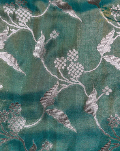 A close-up of teal green fabric with a woven floral pattern in light gray and white.