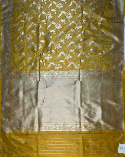 A yellow and gold silk saree with intricate floral motifs woven across the body and a wide beige border, laid flat.