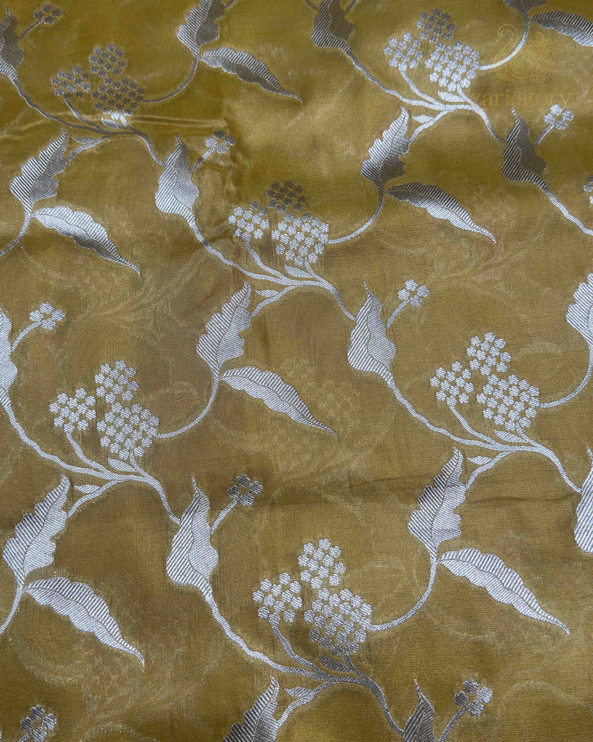 A close-up of a gold-colored sheer fabric with a silver floral and vine pattern woven across it.
