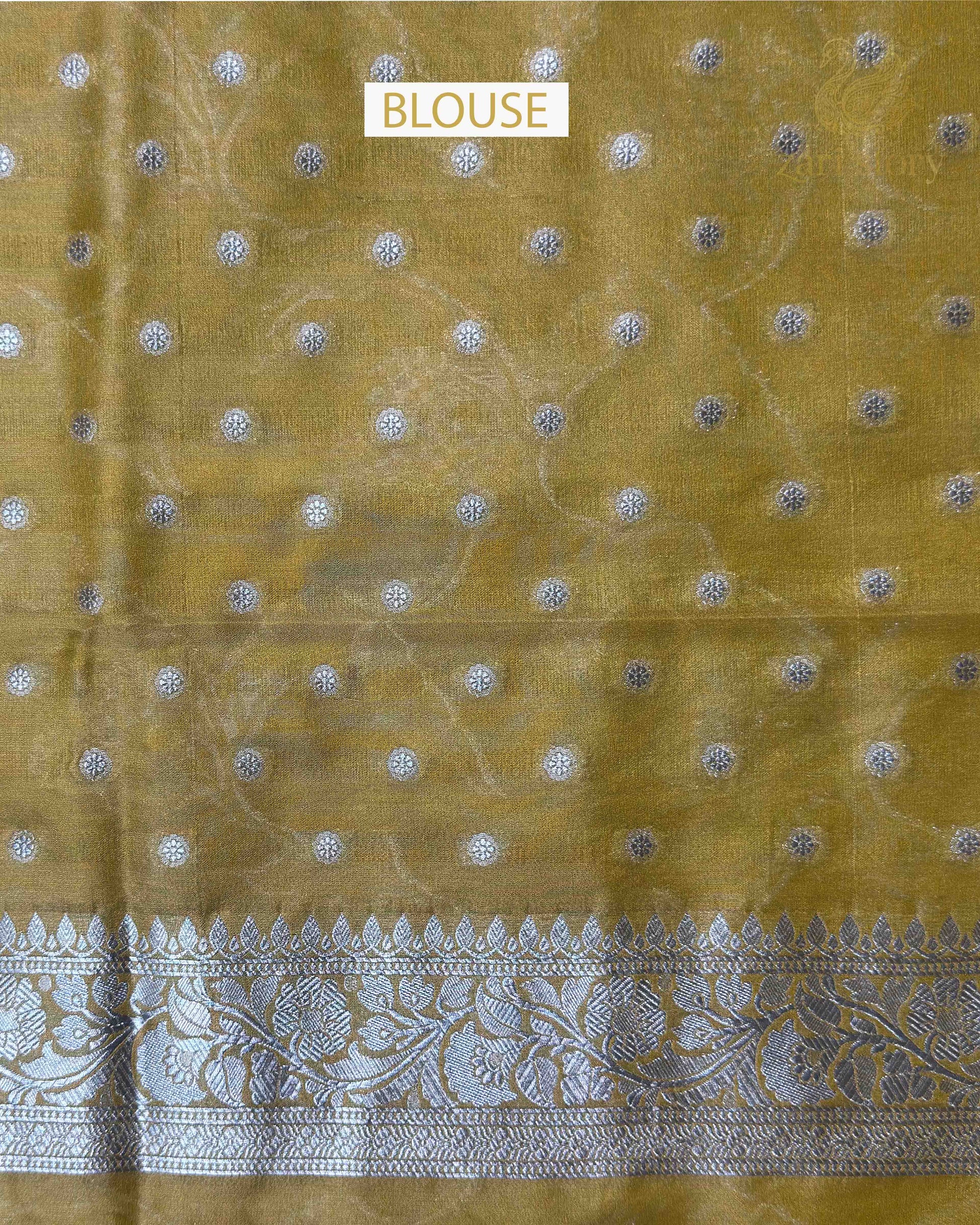 A close-up of a mustard yellow fabric blouse with scattered silver metallic embroidered motifs and a wide ornate silver border along the bottom edge.